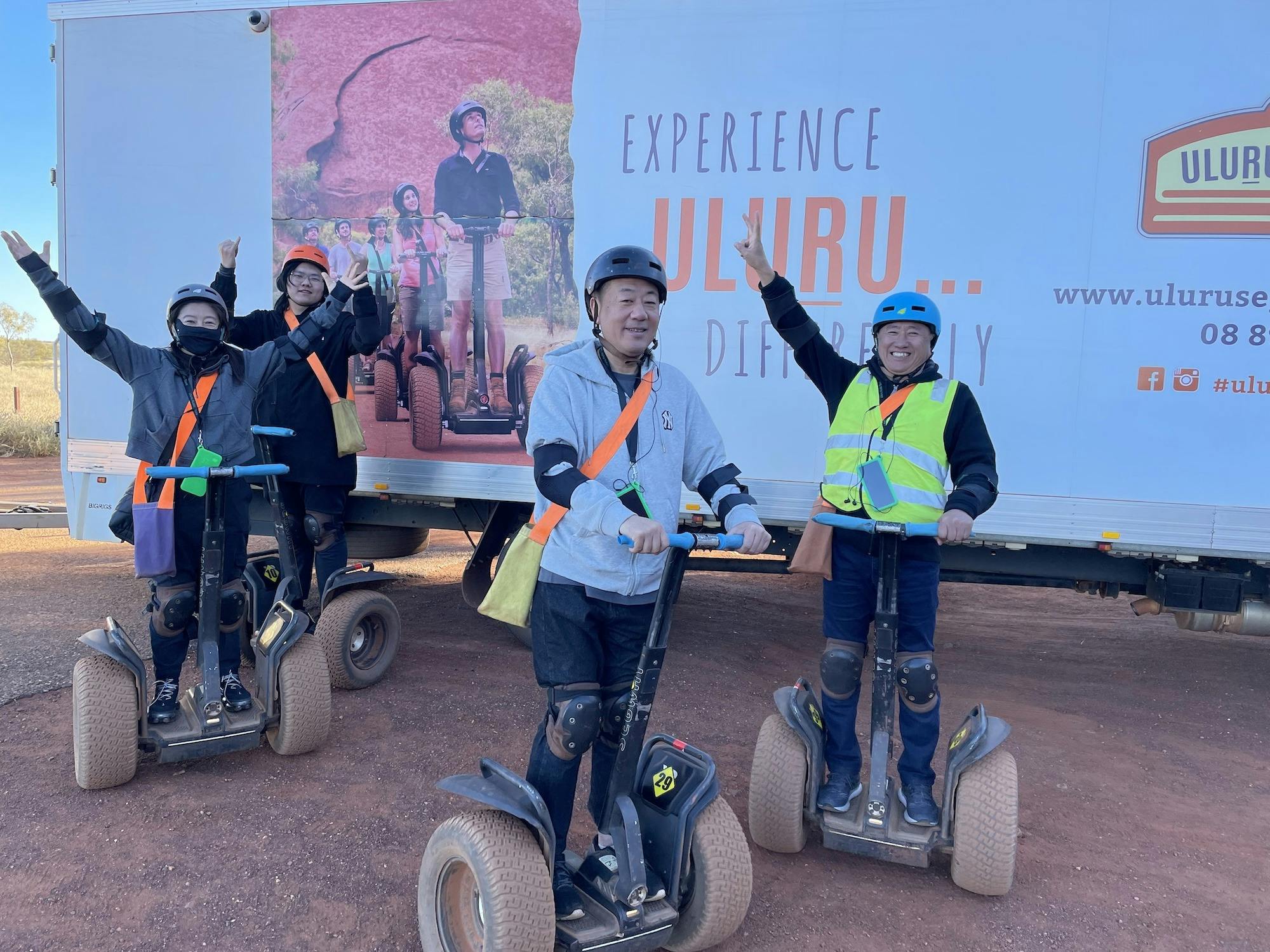 A family group stand on their Segways, each with an arm outstretched cheering. They are having fun.
