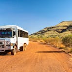 6WD tour coach on a red dirt road and small hill in background