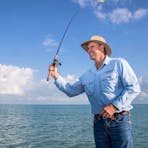 Man with hat fishing on ocean with clouds in background