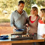 Family barbequing meat using the Ayers Rock Campground facilities