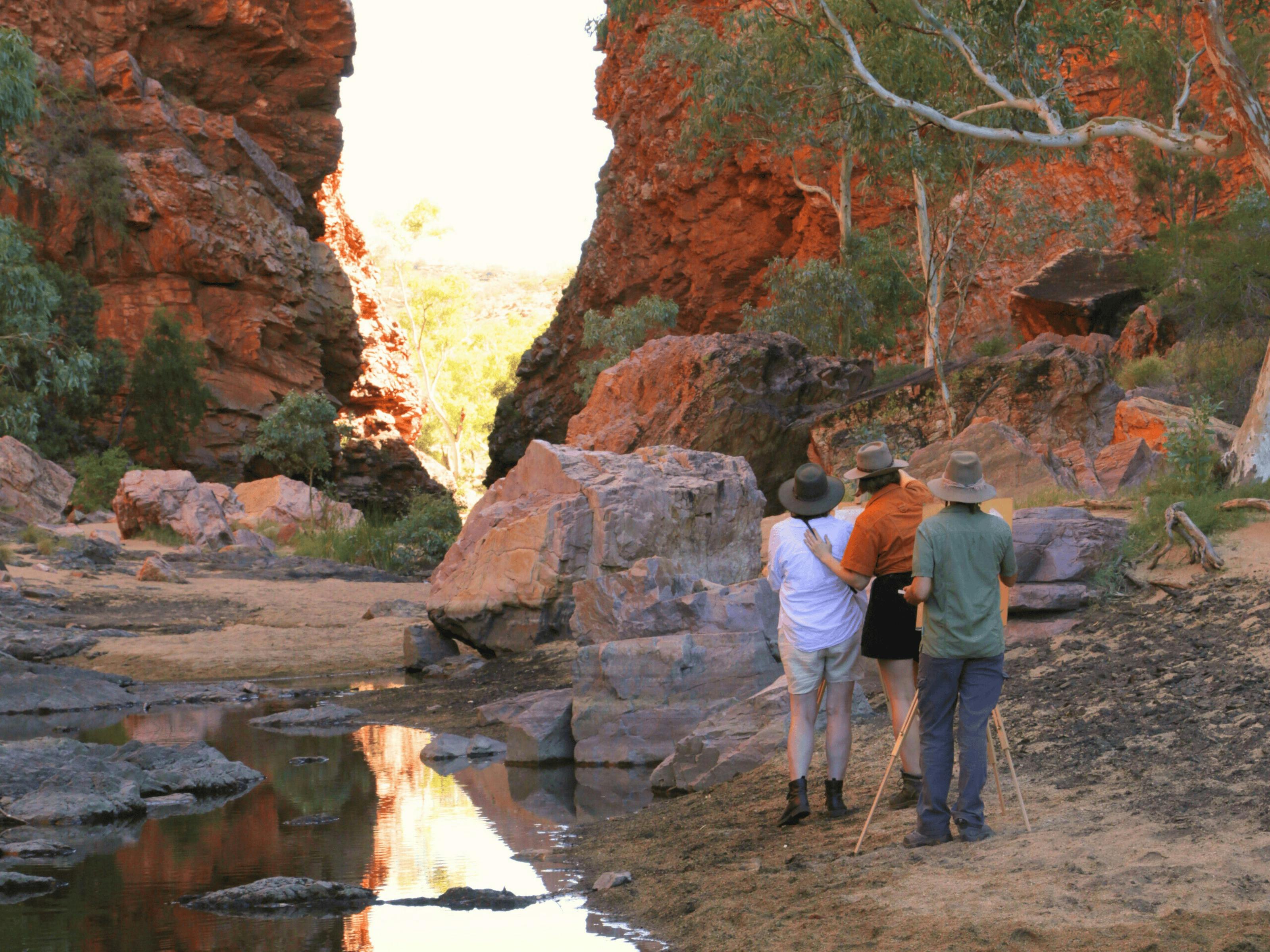three people stand at easels outdoors painting Simpsons Gap