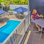 A couple toasting champagne on balcony of an apartment overlooking the swimming pool.