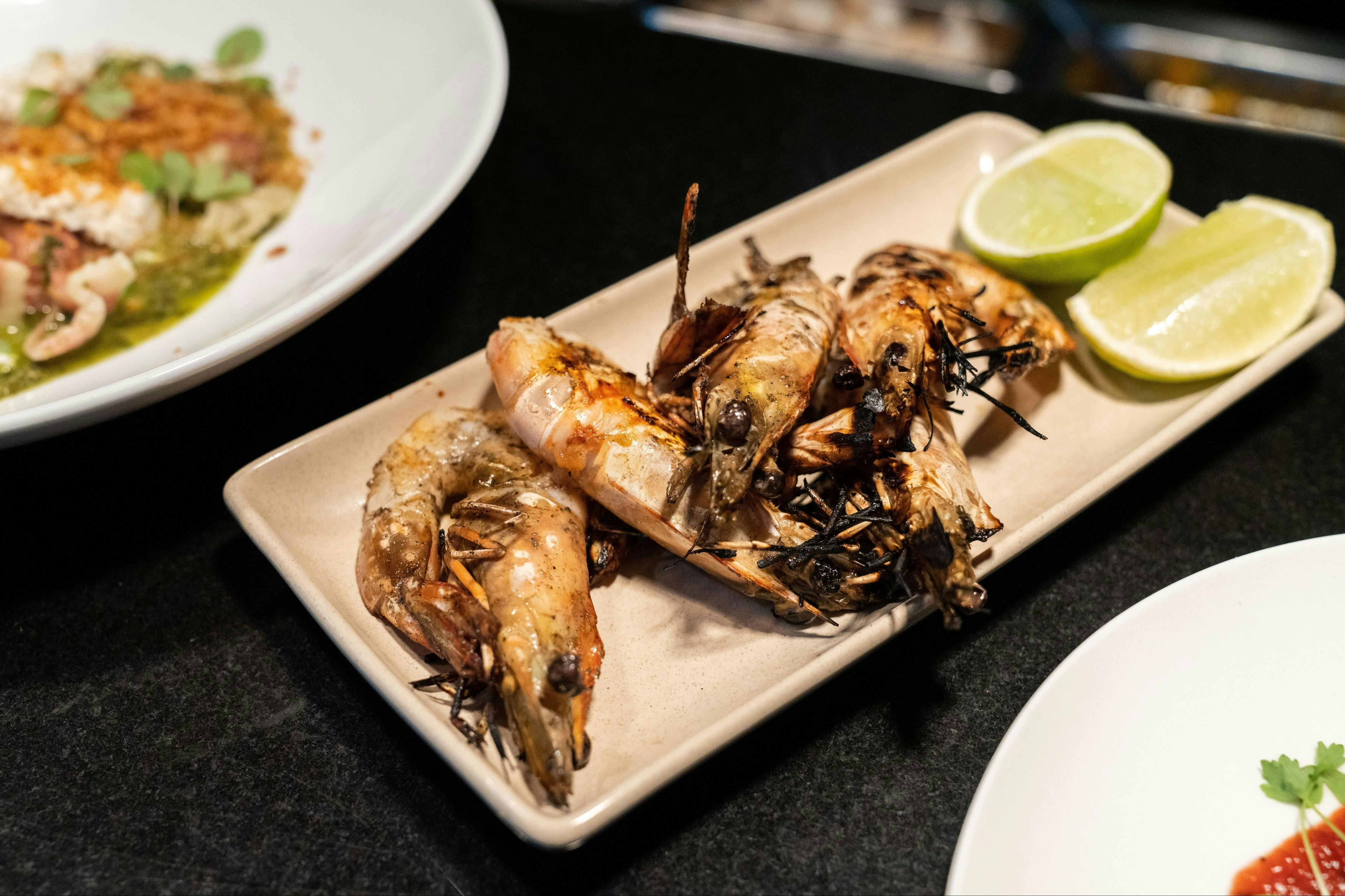 Three whole grilled tiger prawns with charred shells served on a rectangular ceramic plate.