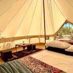 A queensize bed with pillows and linen, a small table with seats on a rug inside a beautiful tent