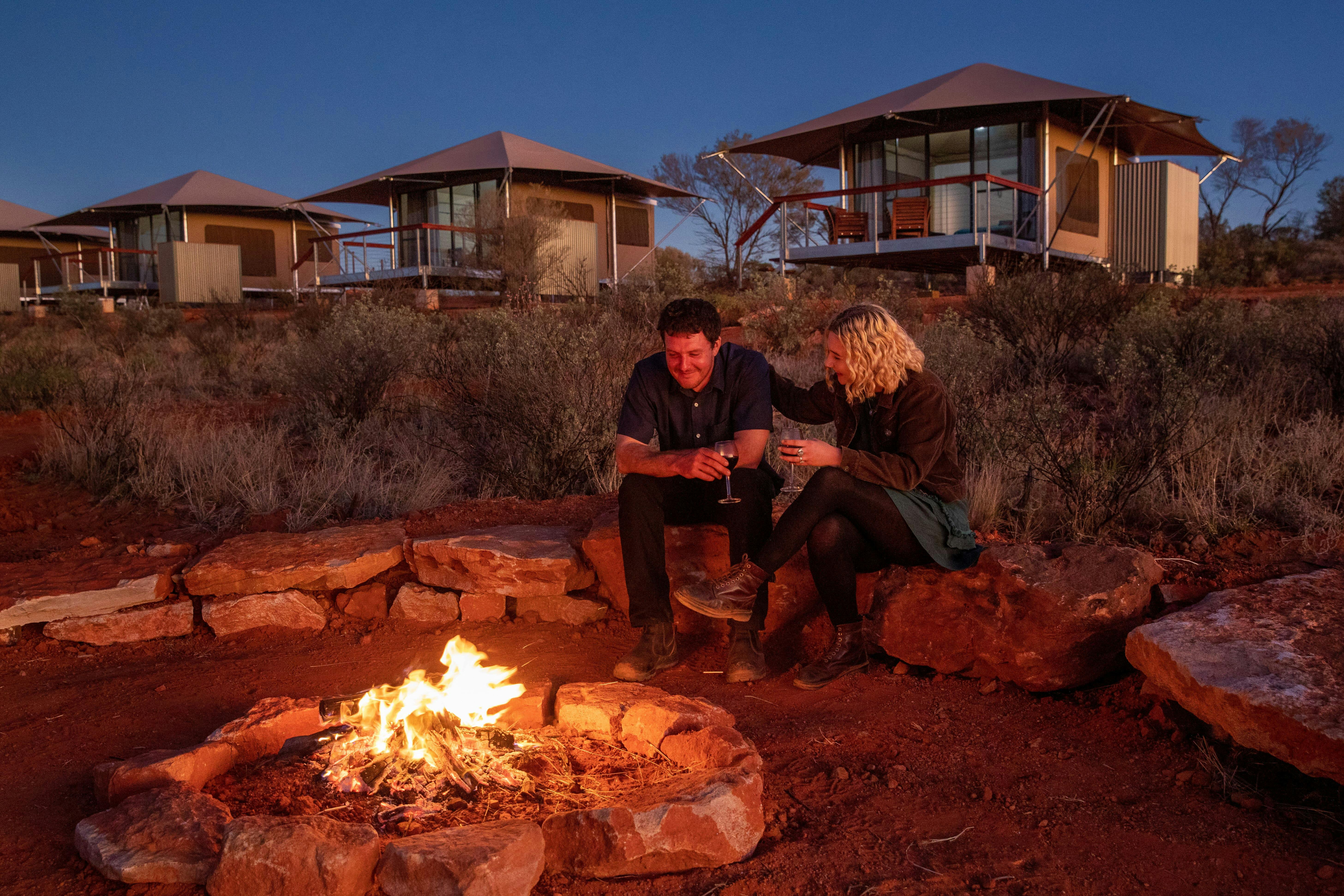 A man and a woman enjoy a wine by the fire at Drovers Dream, Kings Creek Station.
