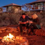 A man and a woman enjoy a wine by the fire at Drovers Dream, Kings Creek Station.