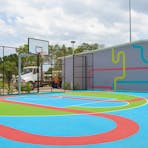 Wide shot of the basketball half court. Text on Brick wall reads “Mates – Play and Have!”