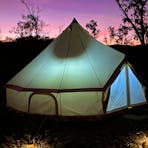 A glamping canvas bell tent sits against a purple evening sky surrounded by solar lanterns