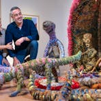 Two people crouching to inspect a colourful woven art installation in a gallery