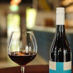 A glass of wine next to it's bottle in a wine barrel