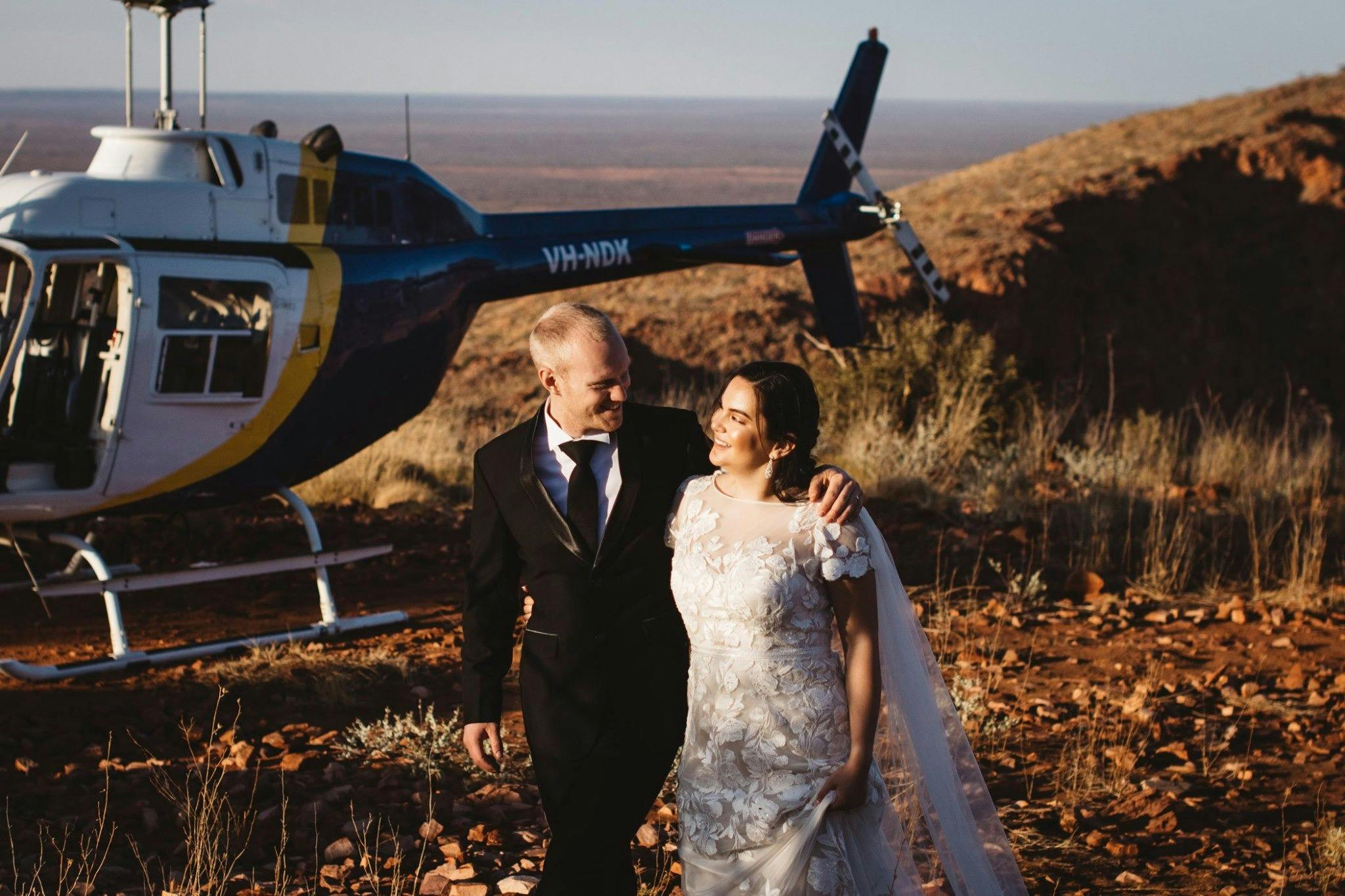 Couples in wedding attire standing next to parked helicopter on a hill