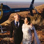 Couples in wedding attire standing next to parked helicopter on a hill