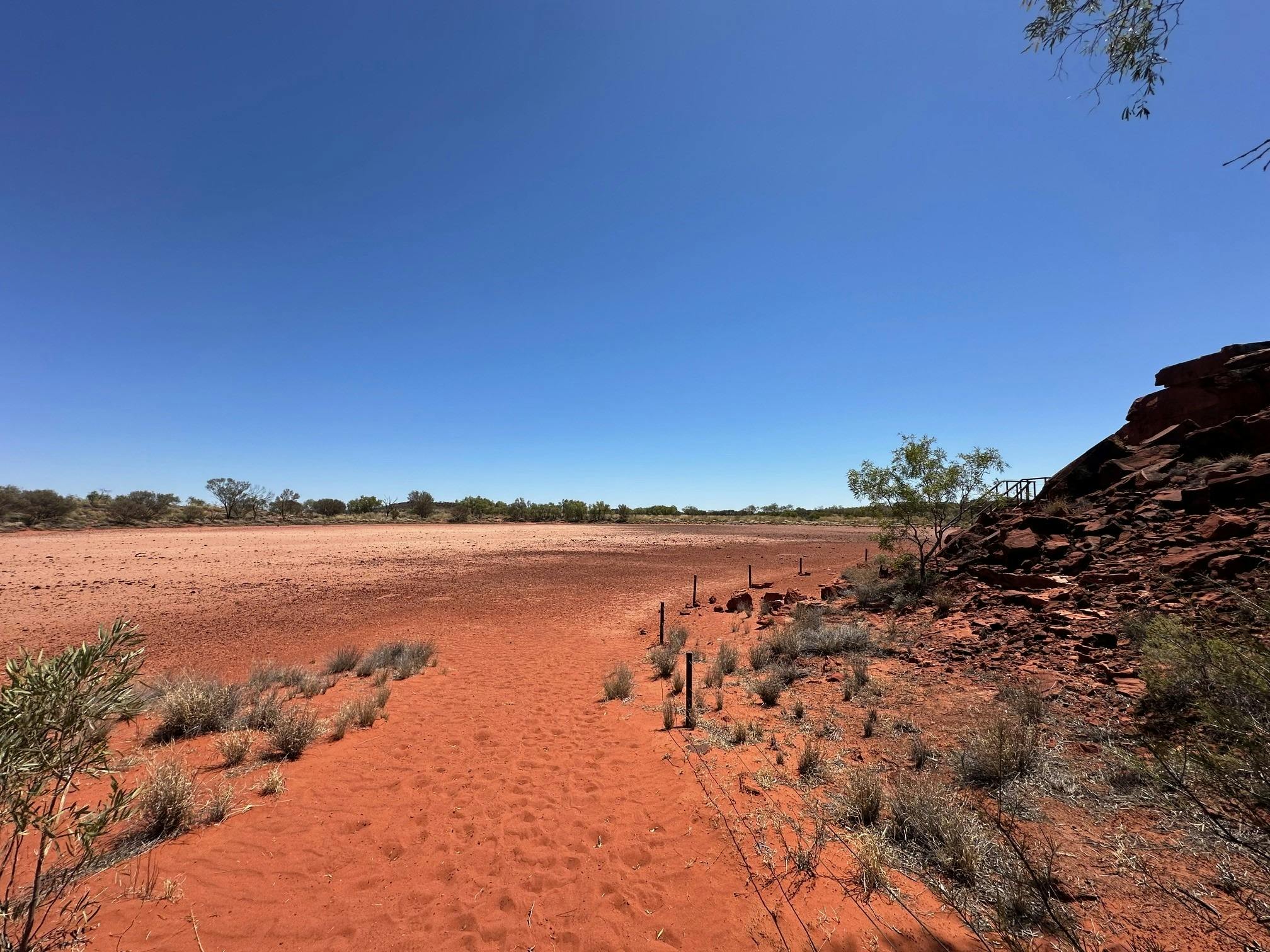 The sandy walking path passes between the rock carvings and the natural claypan