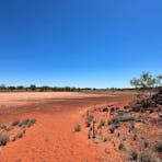 The sandy walking path passes between the rock carvings and the natural claypan