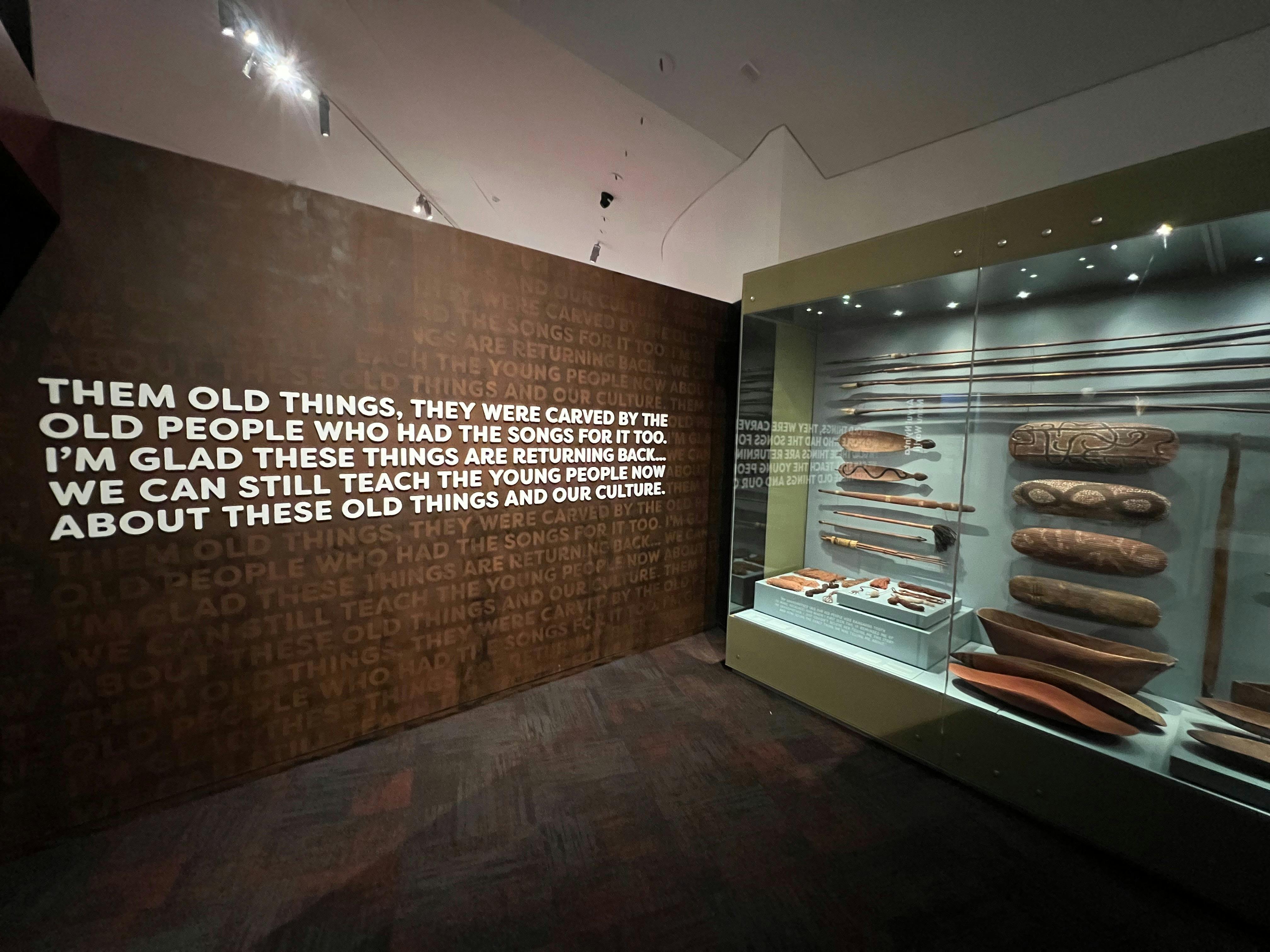 A number of carved wooden objects are housed behind glass on the right. On the left these bold text.