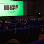 Audiences seated in a dark cinema as the MASIFF festival logo shines on the screen