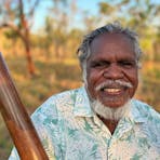 Aboriginal man Manuel Pamkal stands next to a tree with didjeridoo