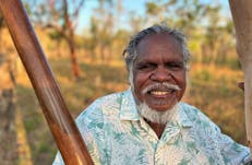 Aboriginal man Manuel Pamkal stands next to a tree with didjeridoo