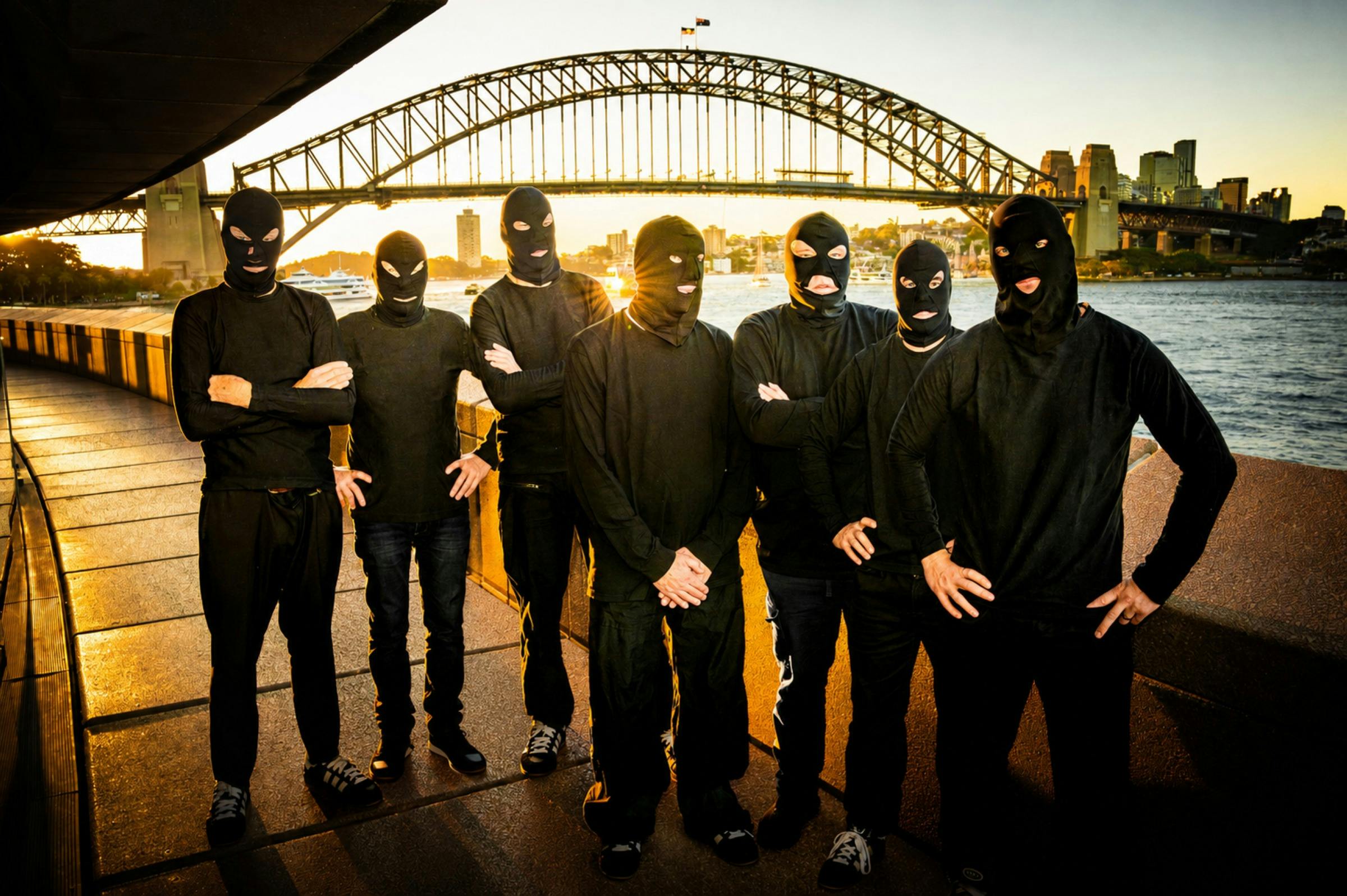 Band members in black costumes, with Sydney Harbour Bridge in the background