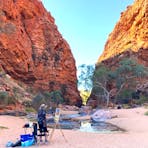 A lady stands at an easel painting the red rocky cliffs at Simpsons Gap