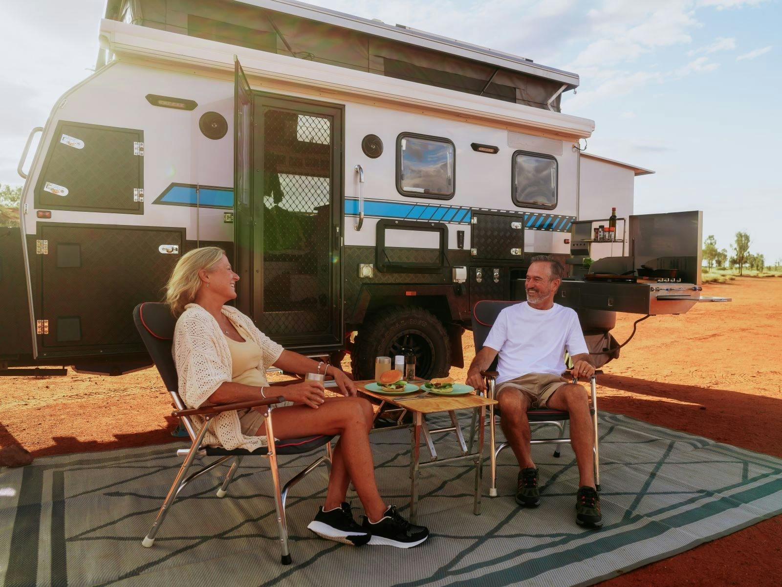 An older couple sitting in front of their caravan chatting