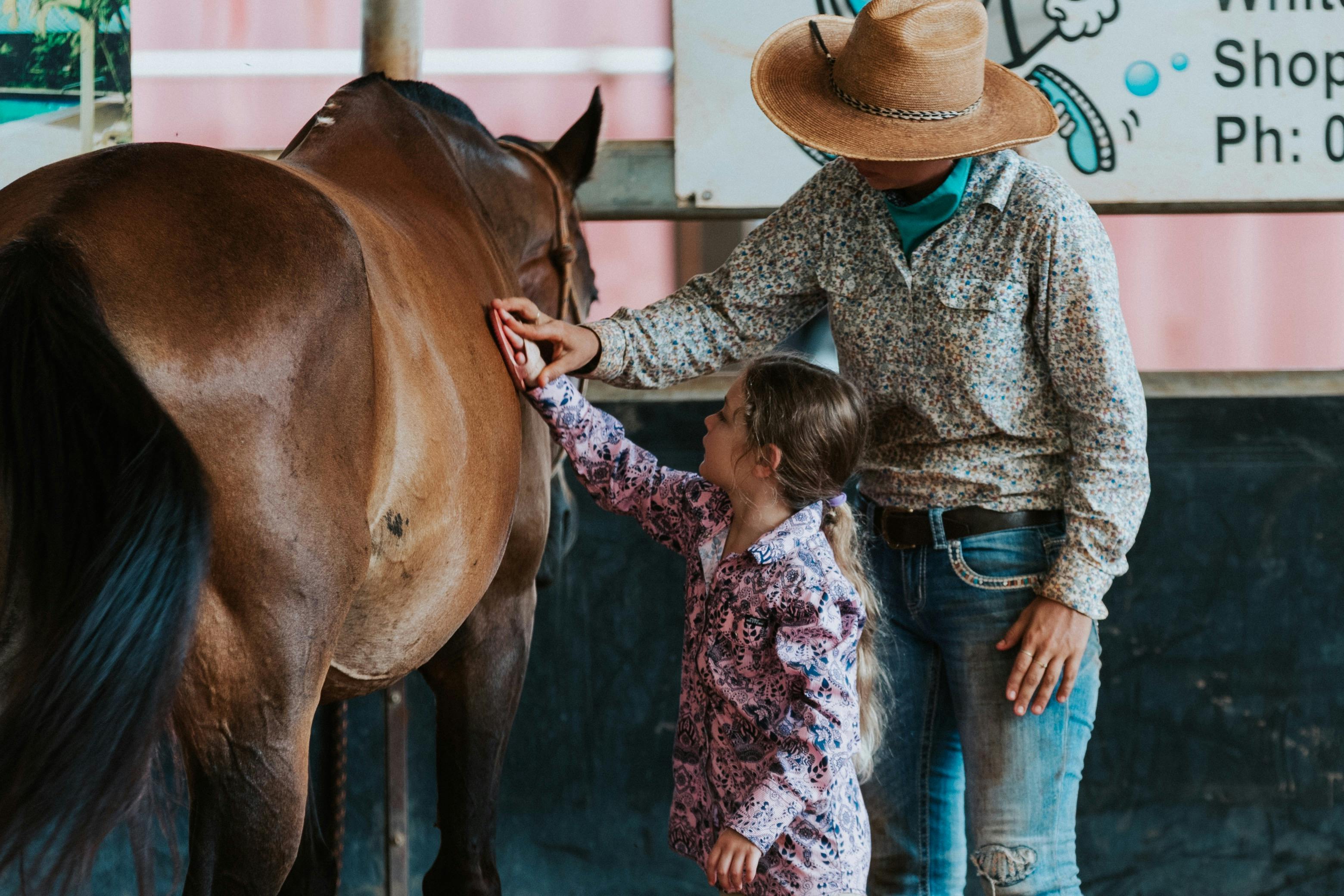 A staff member showing a guest how to brush a horse
