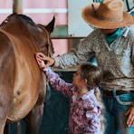 A staff member showing a guest how to brush a horse