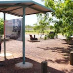 General view of the Attack Creek Memorial roadside stop, with sheltered interpretive signage, camping / picnicking facilities in the background, and the Stuart Highway beyond.