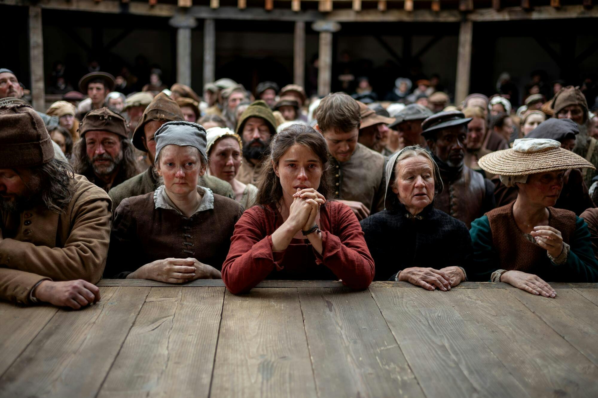 A woman clasps her hands at the front of a crowd at the Globe Theatre.