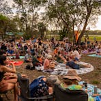 a crowd sitting on the ground outside as the sunsets