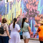 Walk Darwin guide with guests stand before a large multicolour street art mural