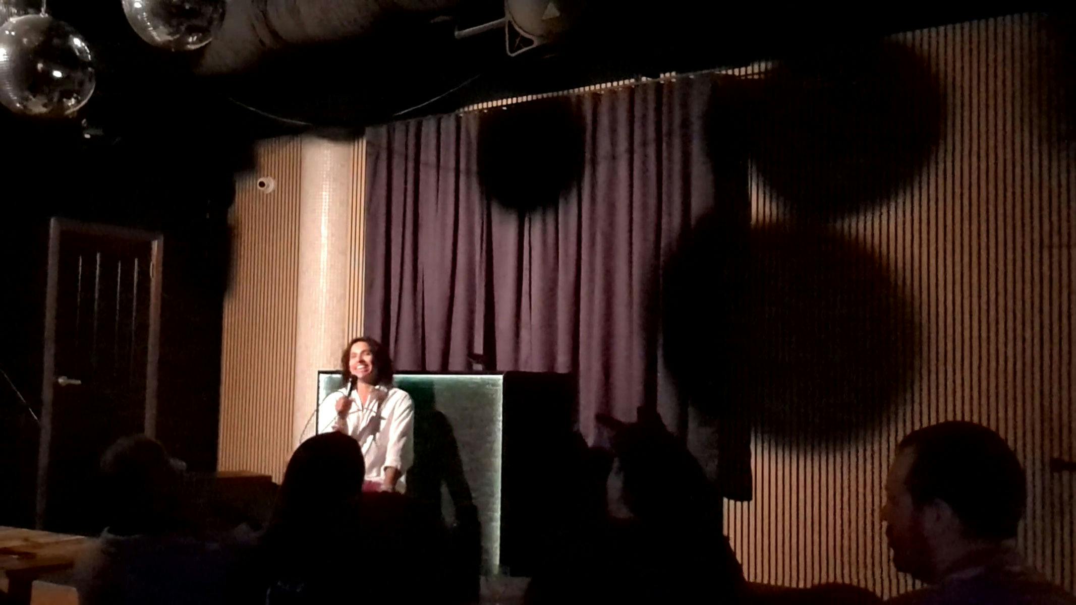 Neptune performing Sex Questions Welcome in Adelaide. Neptune is on stage, in a chair, holding a mic