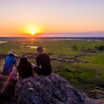 Three people sitting on a rock in Ubirr watching the sunset
