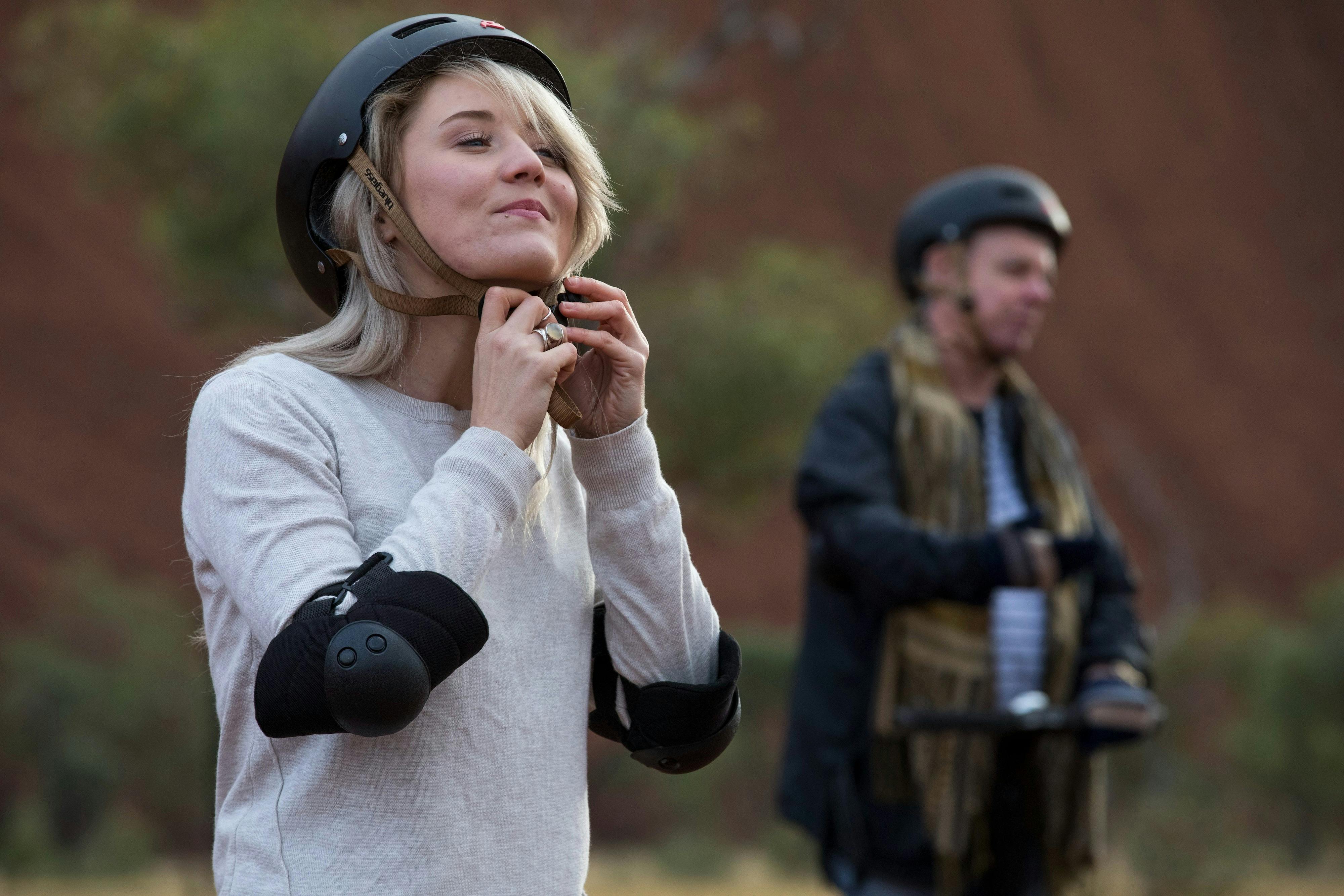A Segway tour participant wears her elbow pads whilst clipping the buckle on her Segway helmet.