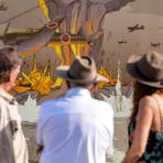 Group of people looking at mural of bombing of Stokes Hill Wharf.