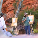 Two people standing painting outdoors with red cliffs and trees
