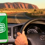 A man drives his car towards Uluru, playing the Uluru Audio Guide device through the car speaker.