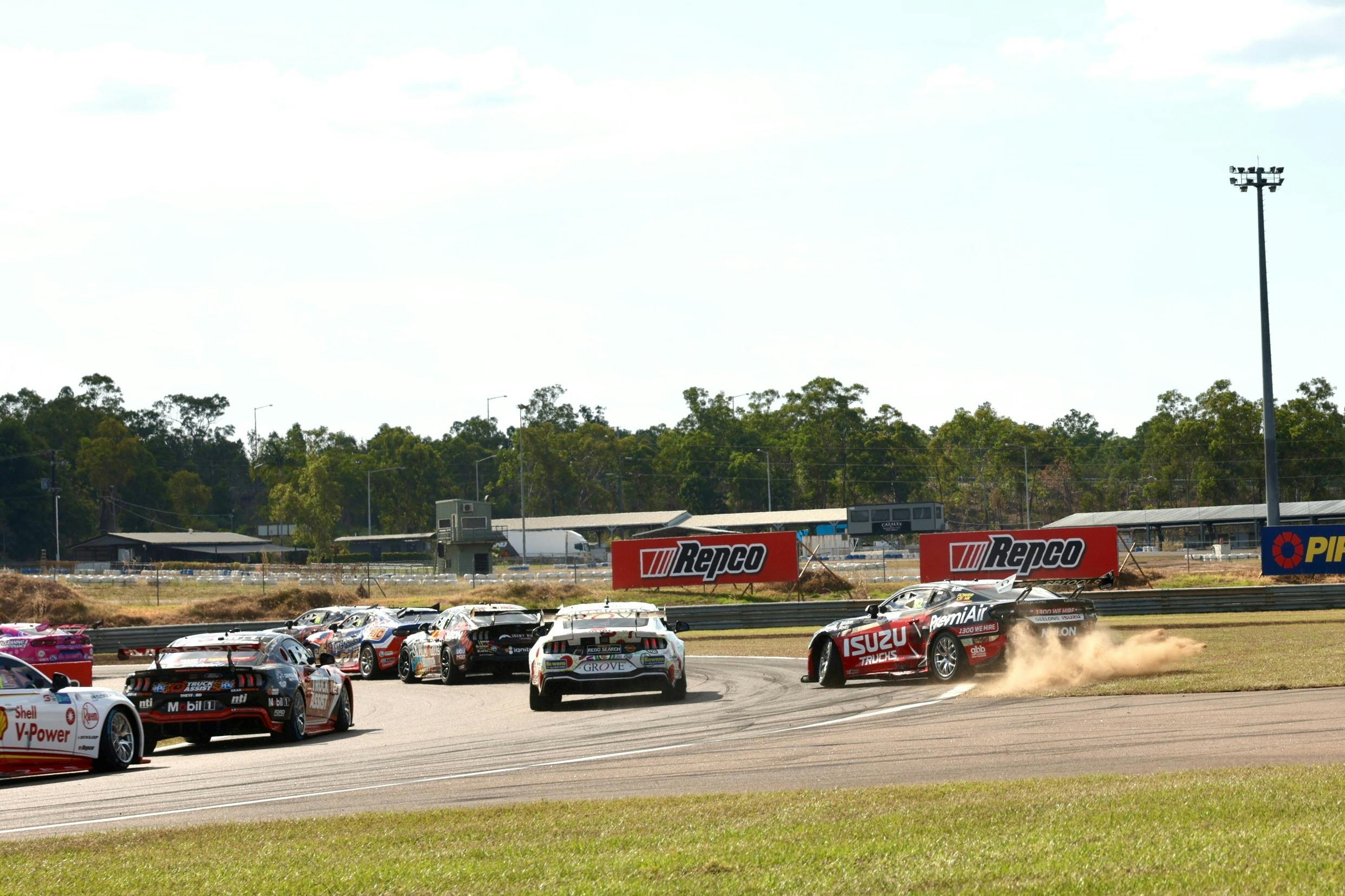 Supercars on track with one car off the track with dust flying from wheels
