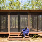 Traditional owner is sitting on the entry steps of the screened kitchen  building where guests cook