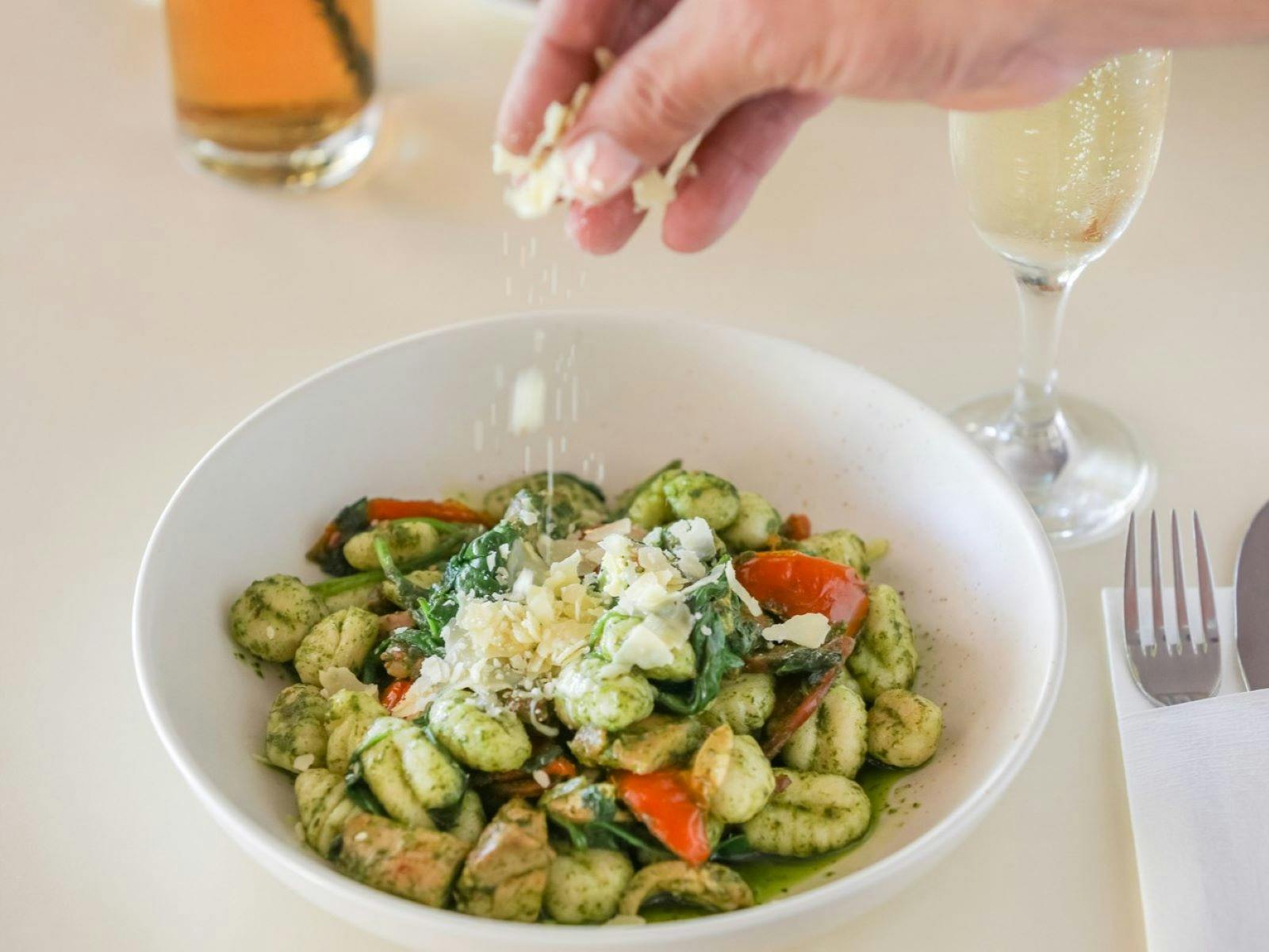 A bowl of chicken alla genovese with gnocci with a hand sprinkling parmesan on top