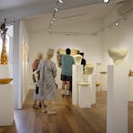 Photograph of people in a small gallery space among various ceramic artworks.