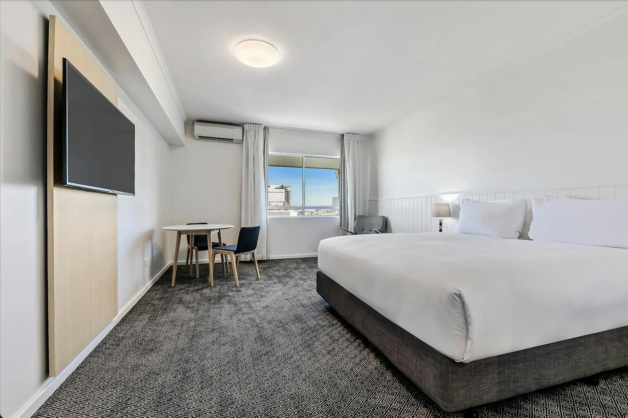 Spacious guest room with king bed, window view, and modern furnishings.