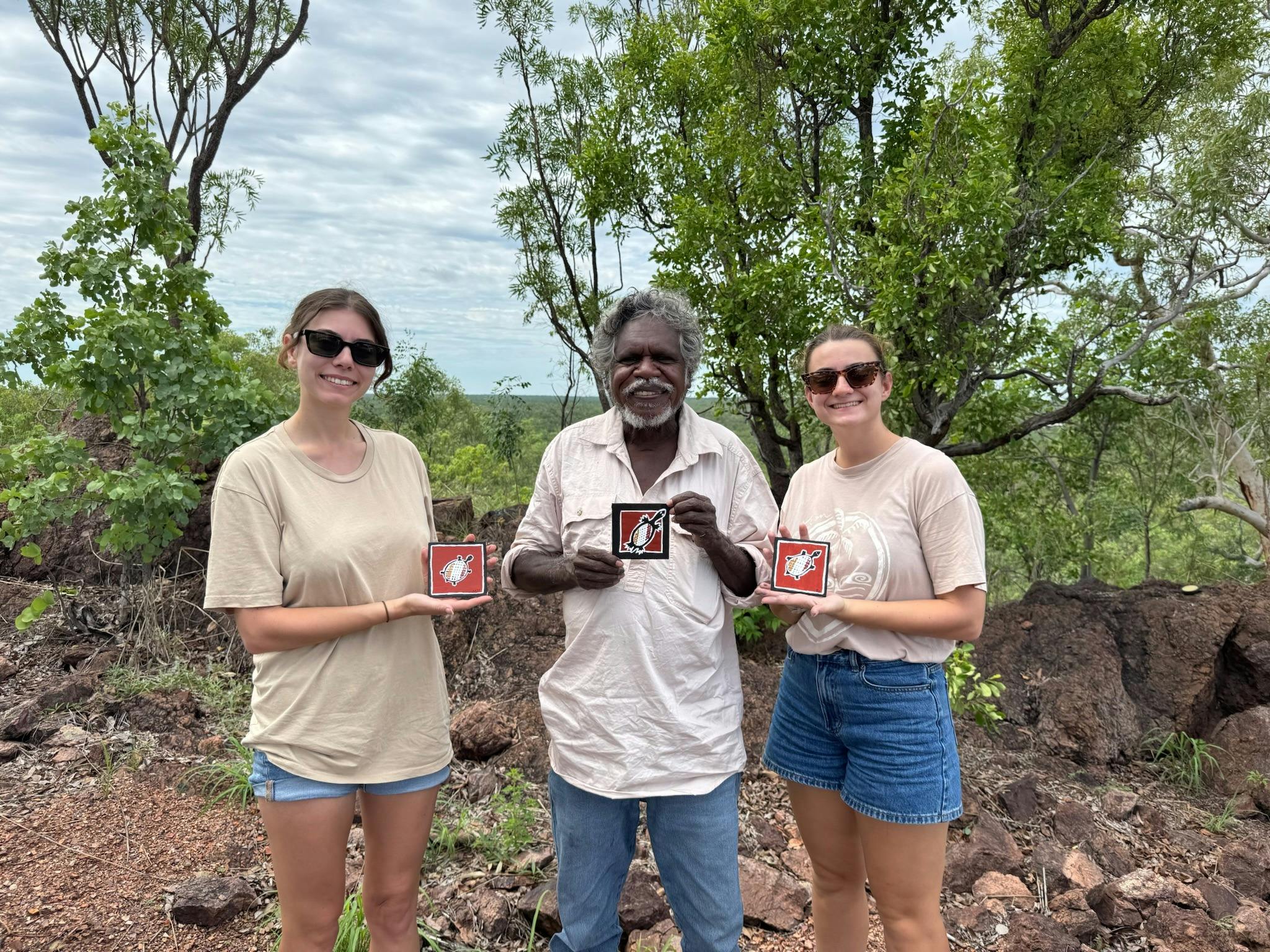 two women stand next to Manuel Pamkal with paintings