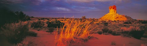 Chambers Pillar at sunset. The large sandstone column rises out of the red desert landscape.