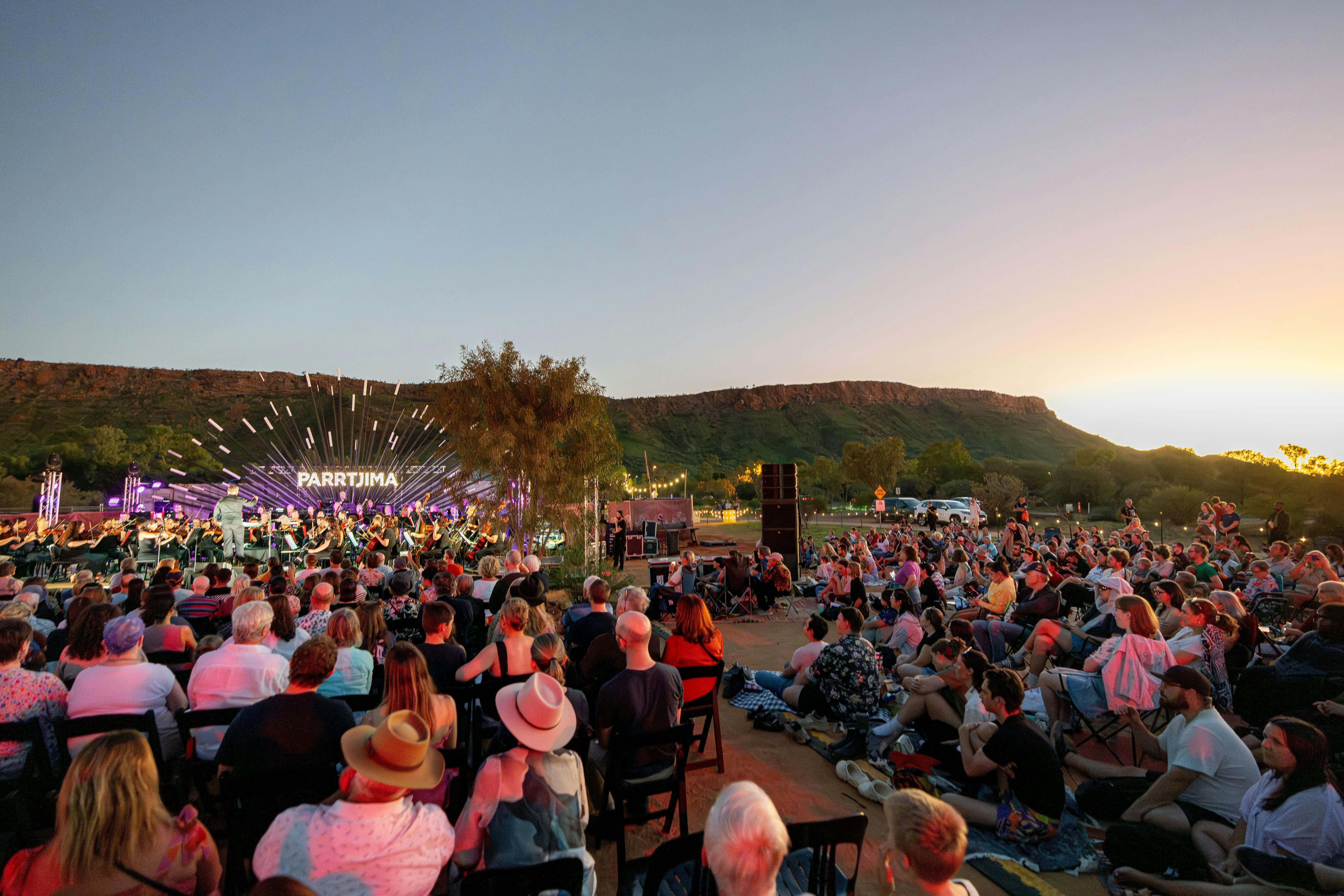 A large crowd watching the Parrtjima stage underneath a setting sun
