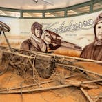 Portraits of Hitchcock and Anderson behind remains of their plane in diorama