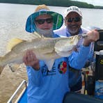Two men standing in a boat holding a barramundi.