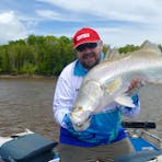 Greg Ireland standing in the boat holding a big barramundi.