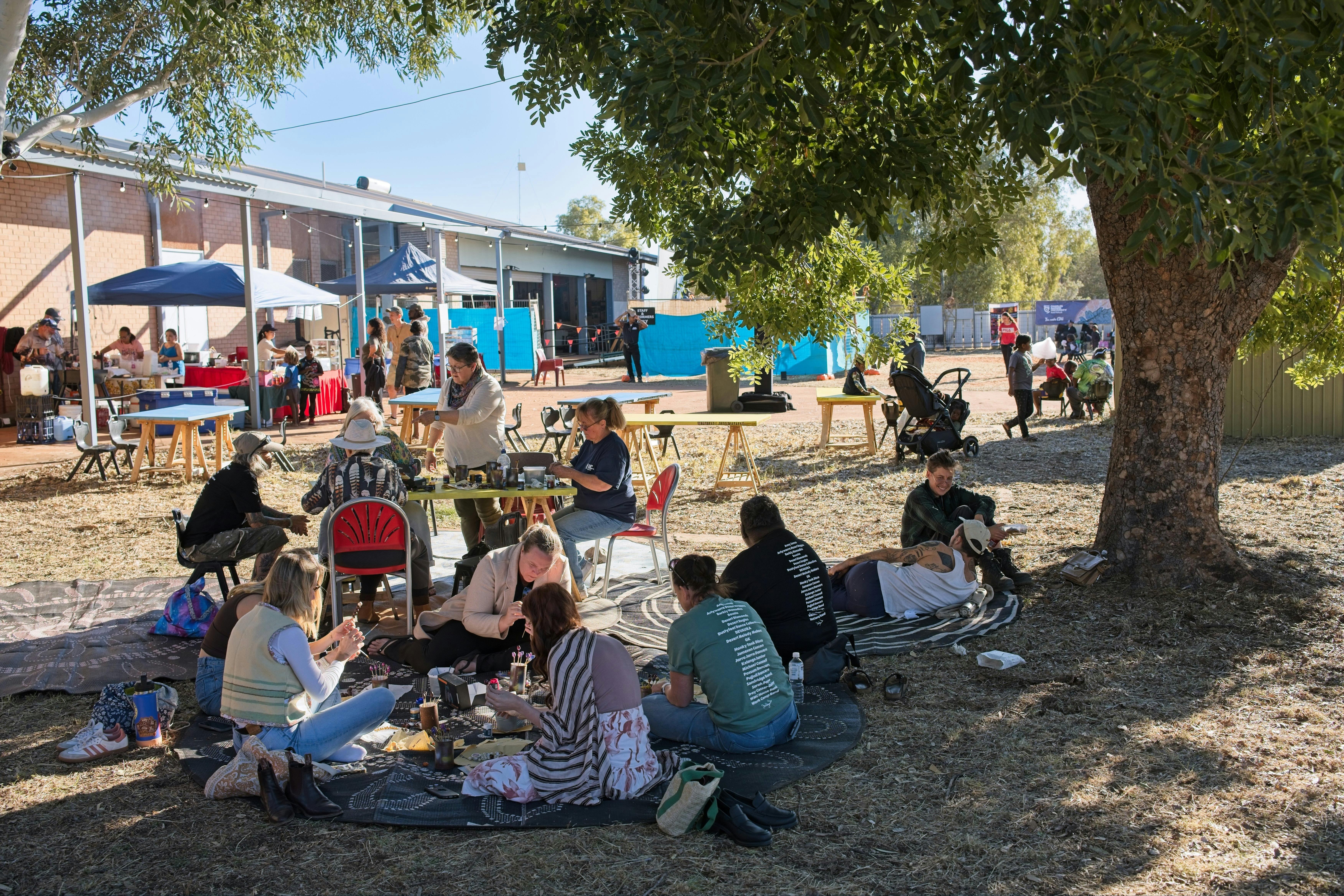 Attendees sitting on the ground and around a table painting  bush seeds