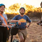 A couple stand on their Segways looking up at Uluru, whilst their guide teaches them about Uluru